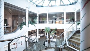A multi-level atrium with glass ceilings, indoor plants, and modern furnishings. - DEKRA Congresshotel Wart (Altensteig)