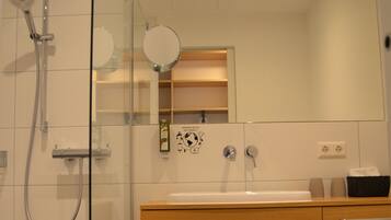 A modern bathroom with a glass shower enclosure, a wooden vanity with a mirror, and a white sink.