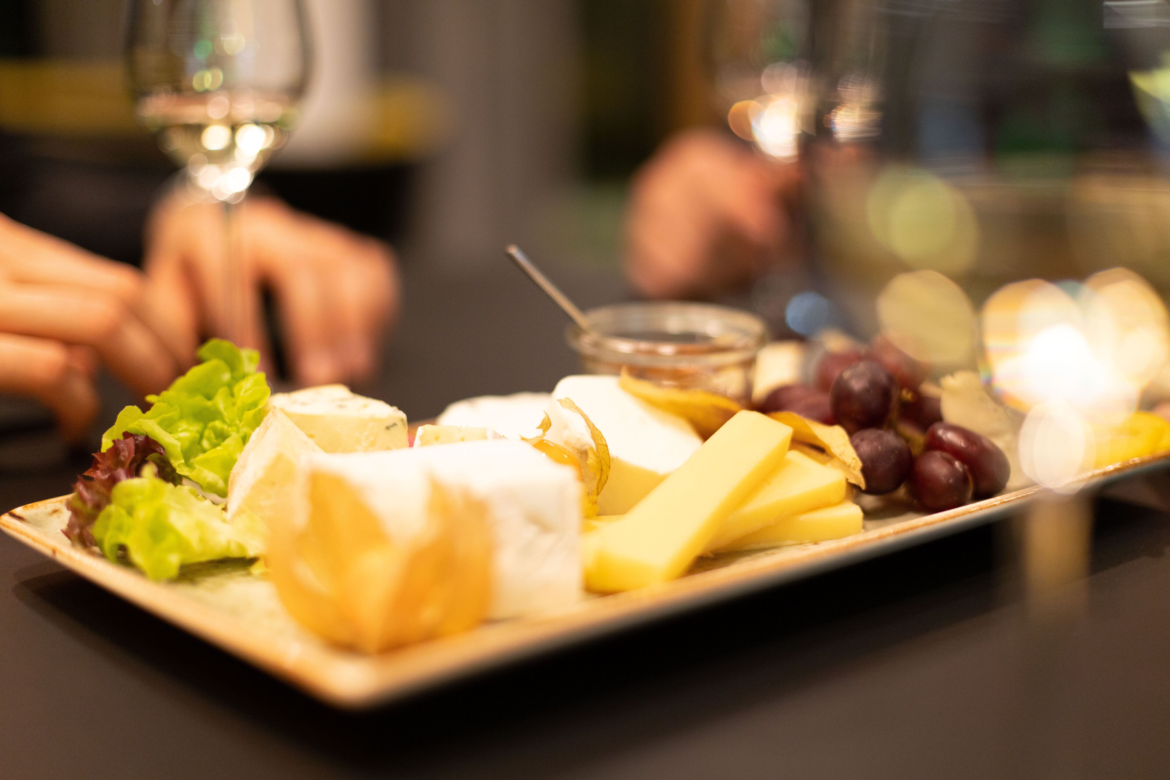 A cheese board with various cheeses, grapes, and a small bowl of honey.
