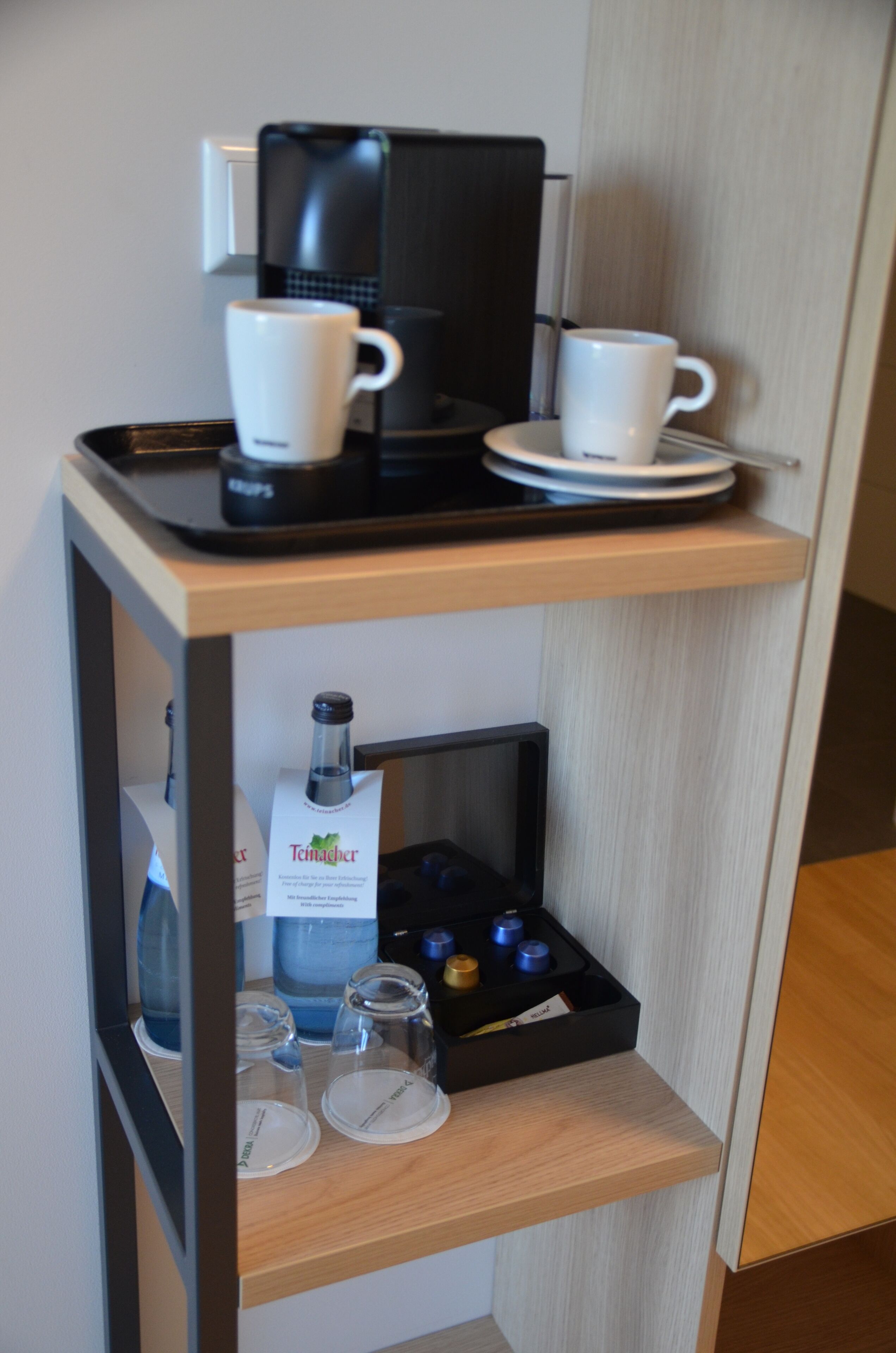 A hotel room's minibar with a coffee maker, two cups, glasses, and a bottle of water.