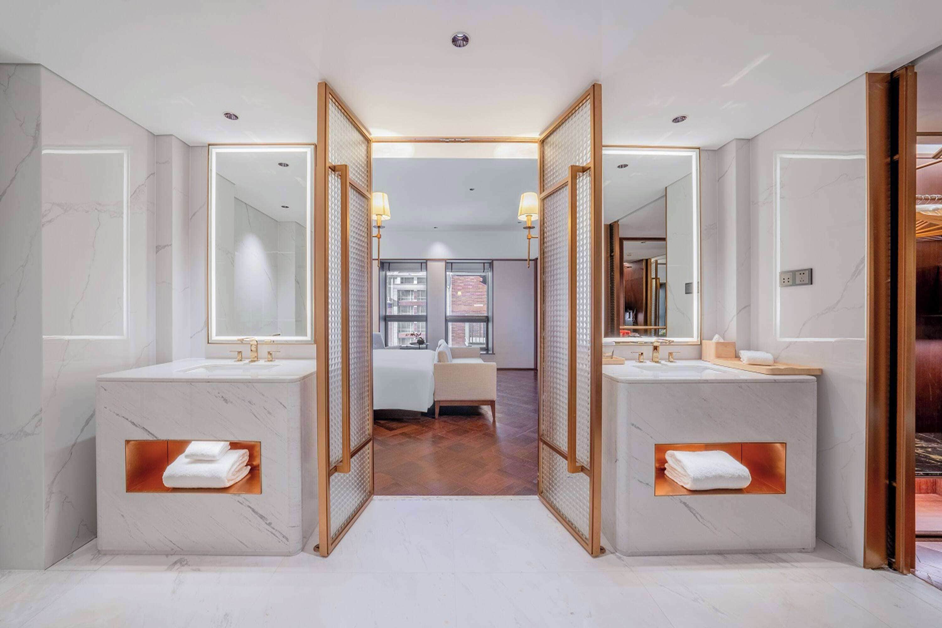 Un baño moderno con dos lavamanos, un espejo grande y vista a un dormitorio.