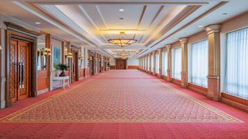 A long hallway with a red carpet, large windows, and a chandelier.