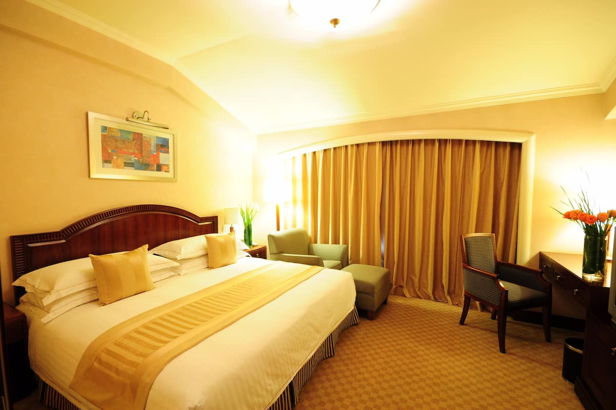 A hotel room with a large bed, a desk, a chair, and a window with curtains.