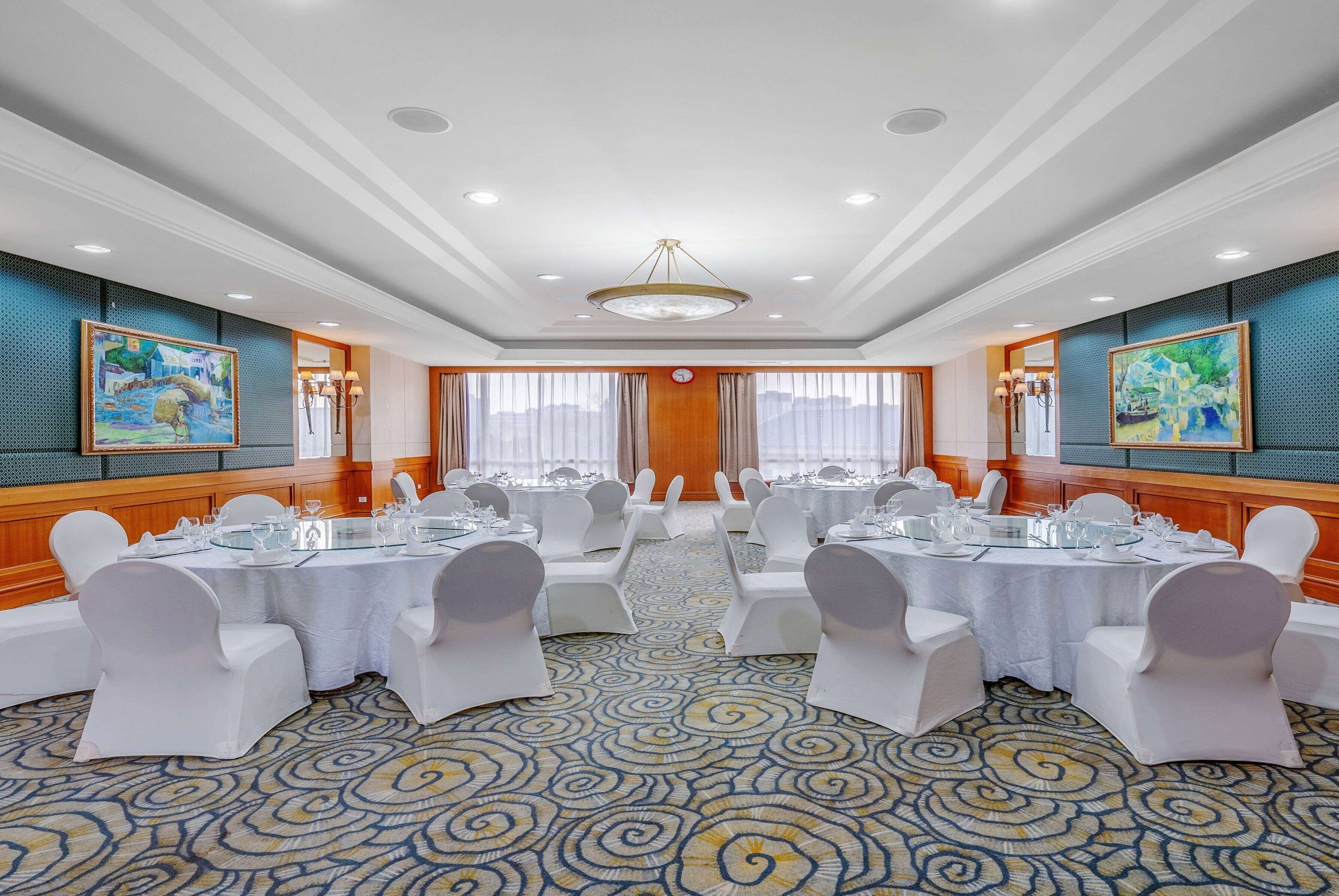 A conference room with round tables, white chairs, and a patterned carpet.