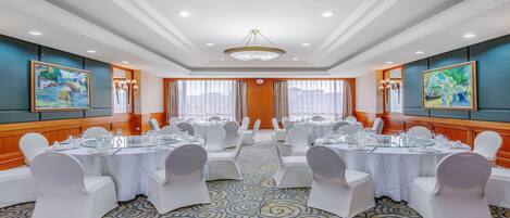 A conference room with round tables, white chairs, and a patterned carpet.