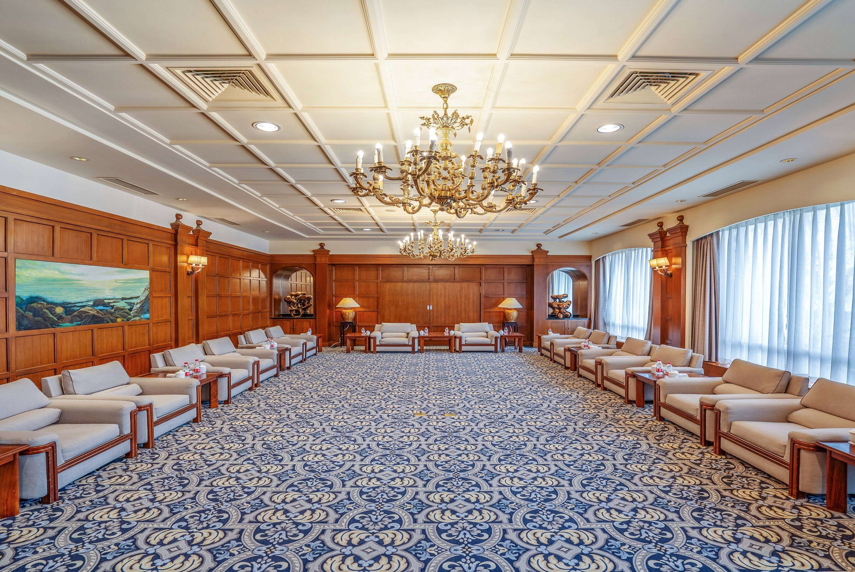 Una amplia sala de conferencias con alfombra estampada, paneles de madera y una gran lámpara de araña.