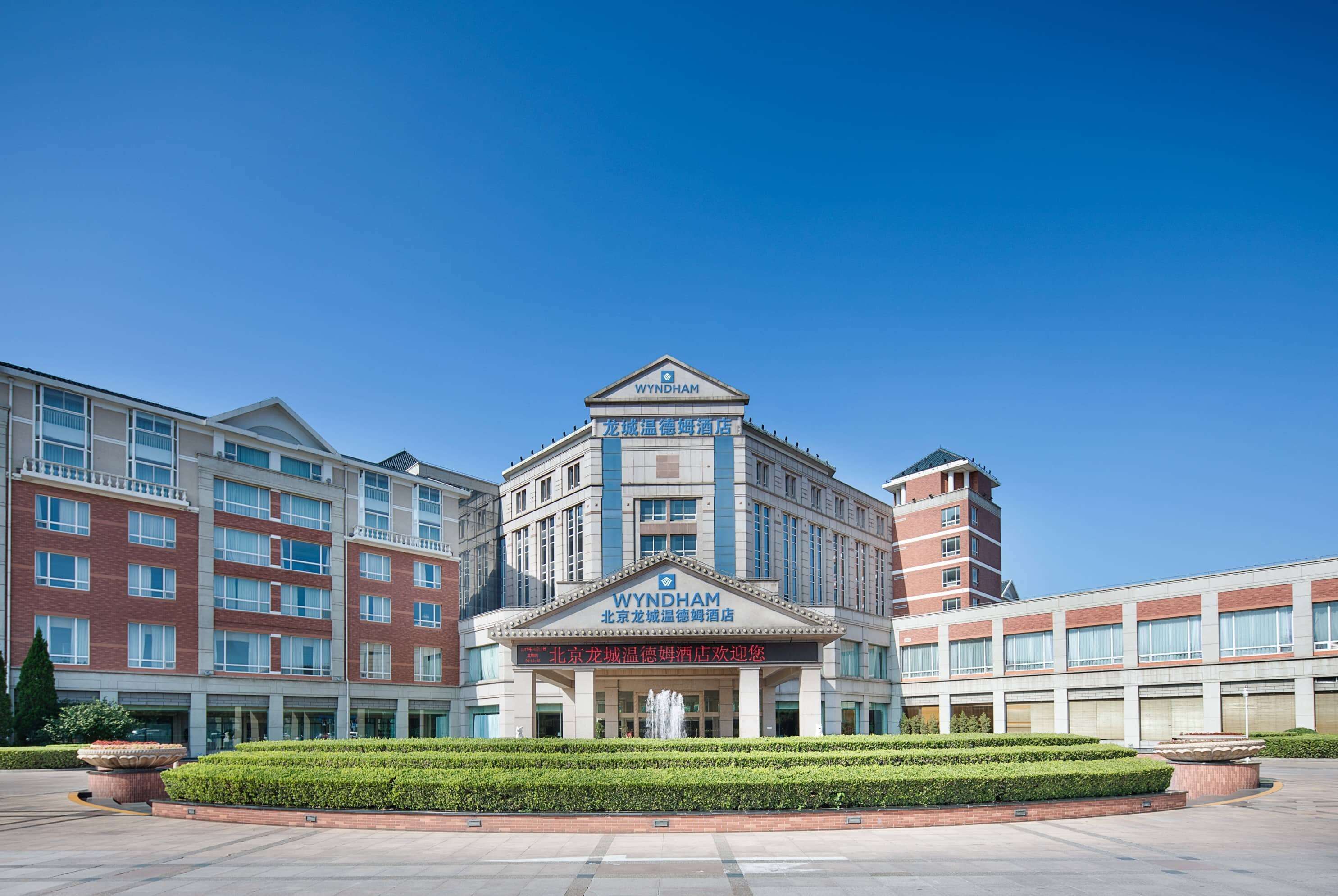 A multi-story hotel with a prominent WYNDHAM sign, featuring a classical architectural style with a central entrance and a landscaped courtyard.