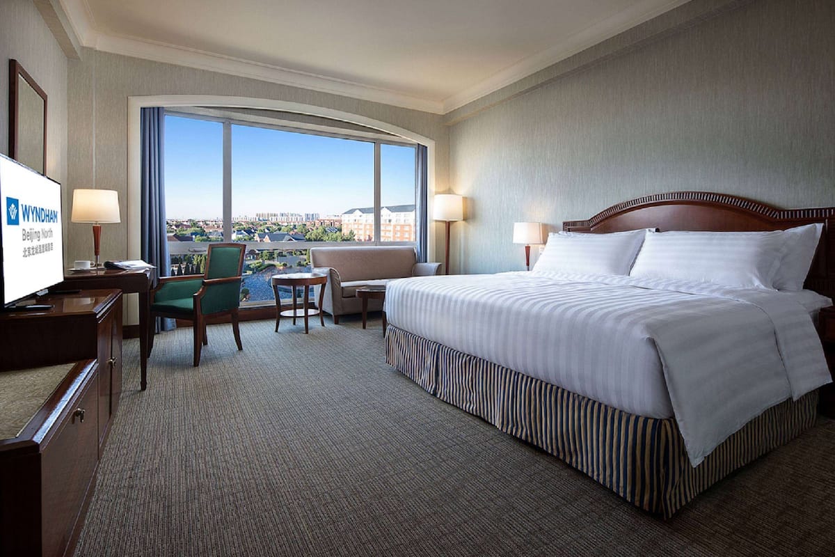 A hotel room with a large bed, two chairs, a desk, and a television.