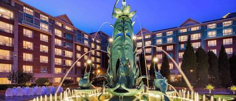 A fountain with a bird sculpture in the center, surrounded by a pool of water, with a hotel building in the background.