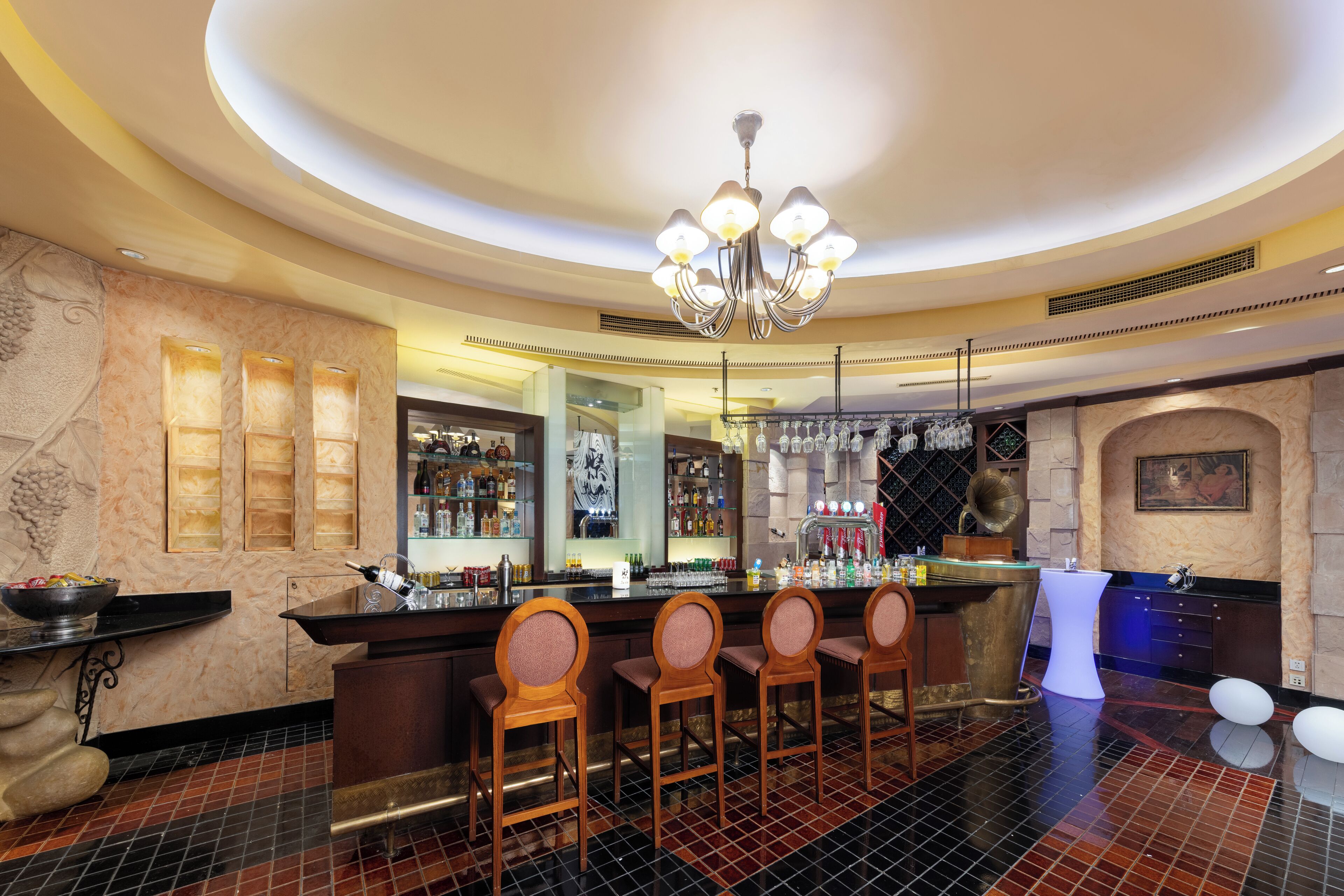 A bar area with a modern chandelier, bar stools, and a counter with a wine cooler.