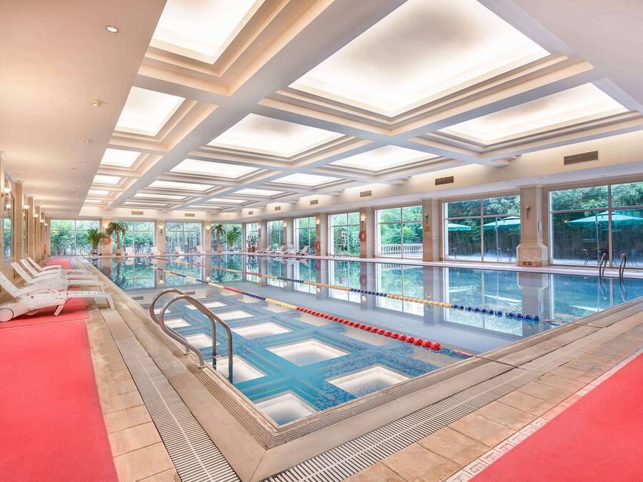 An indoor swimming pool with clear glass walls, a red carpet, and a tiled floor.