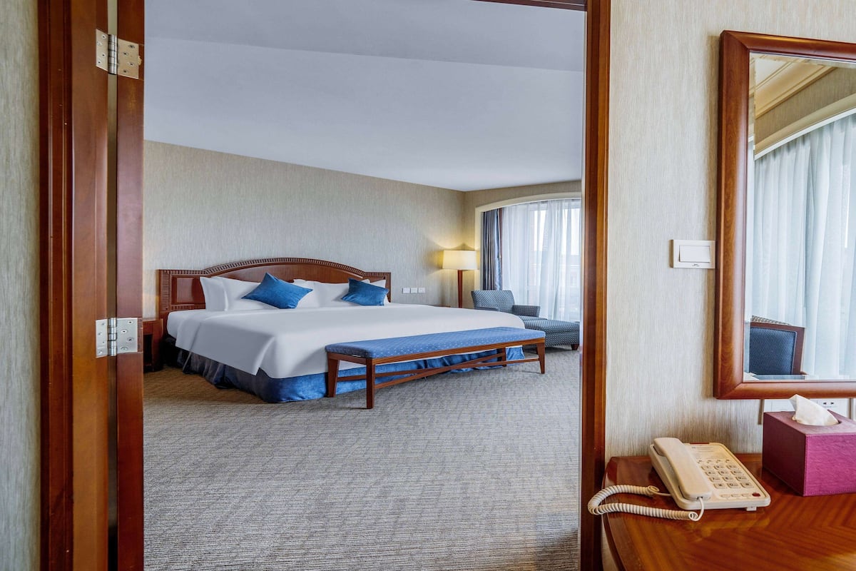 A hotel room with a large bed, a bedside table with a telephone, a lamp, and a mirror.