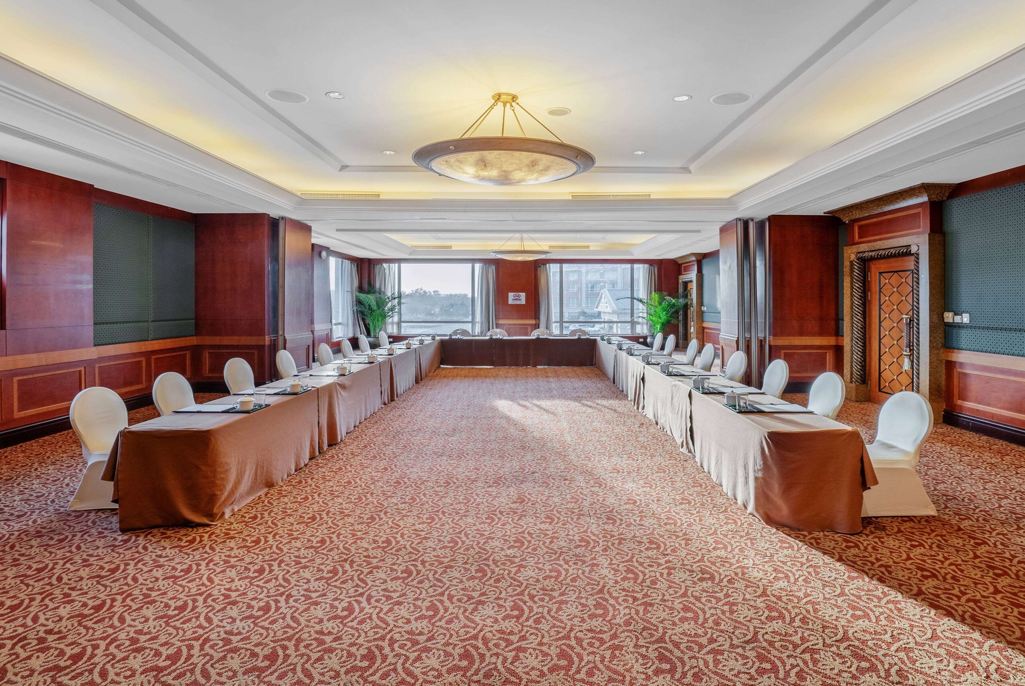 Un salón de conferencias con una larga mesa, sillas blancas y una alfombra estampada.