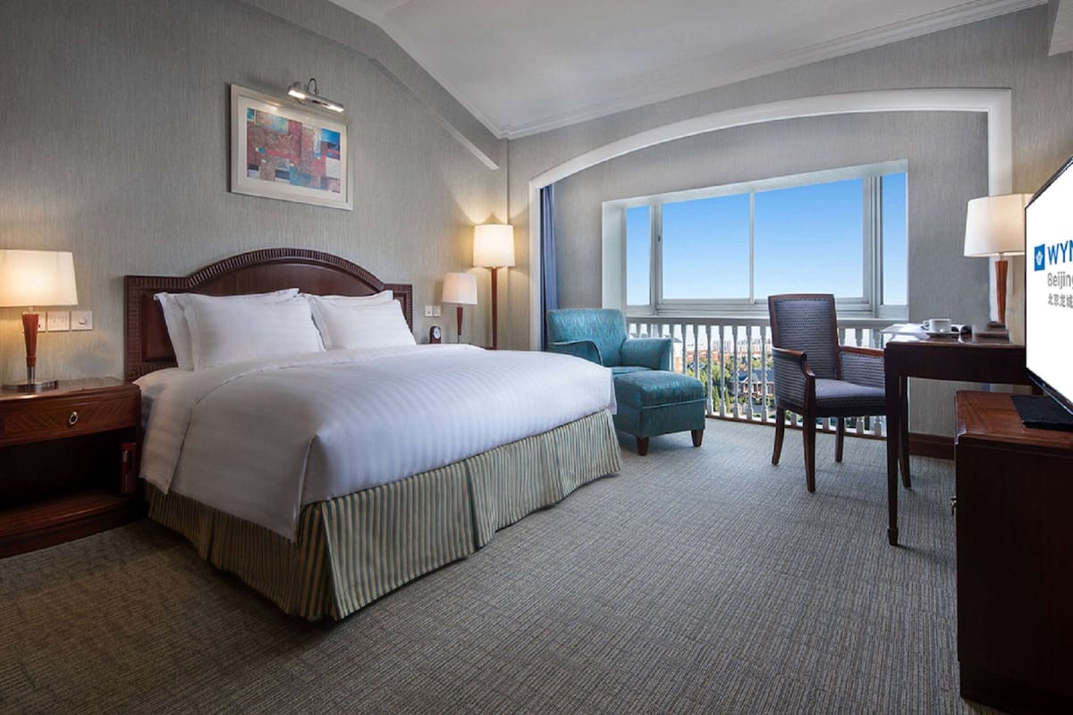 A hotel room with a large bed, two chairs, a desk, and a balcony with a view.