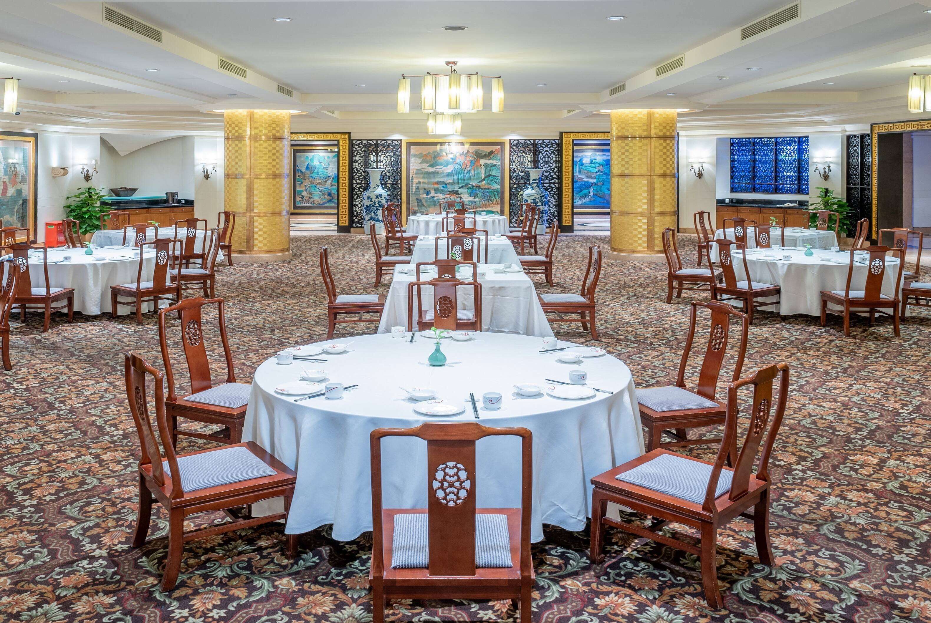 A banquet hall with round tables, wooden chairs, and a carpeted floor.