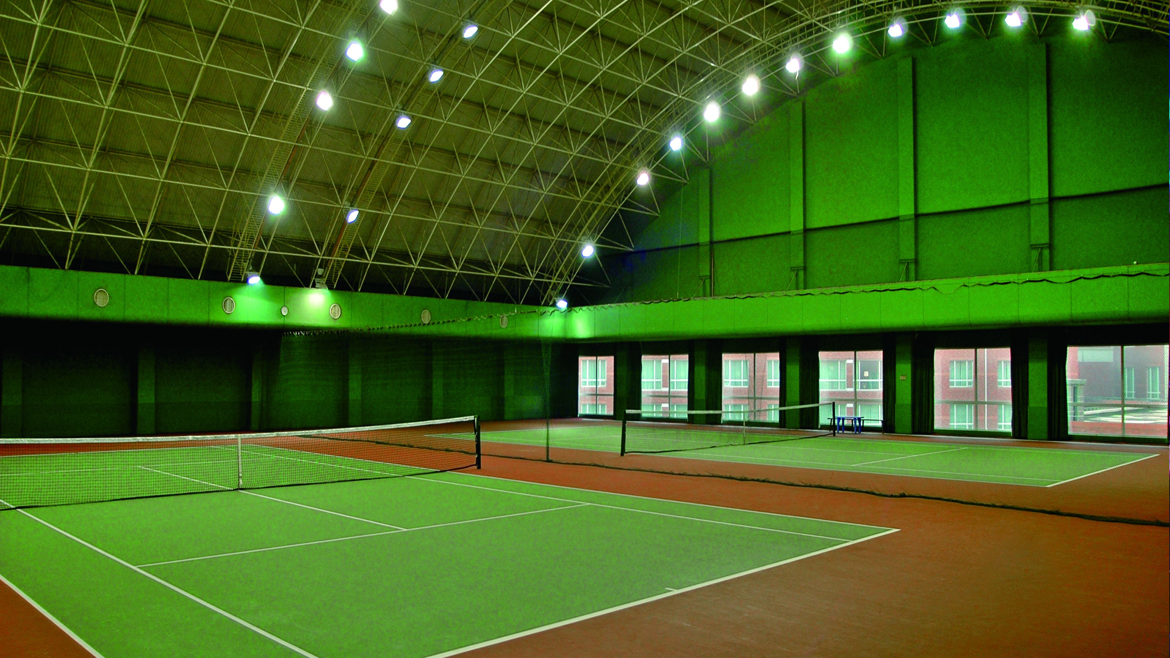 An indoor tennis court with a green roof and multiple courts.