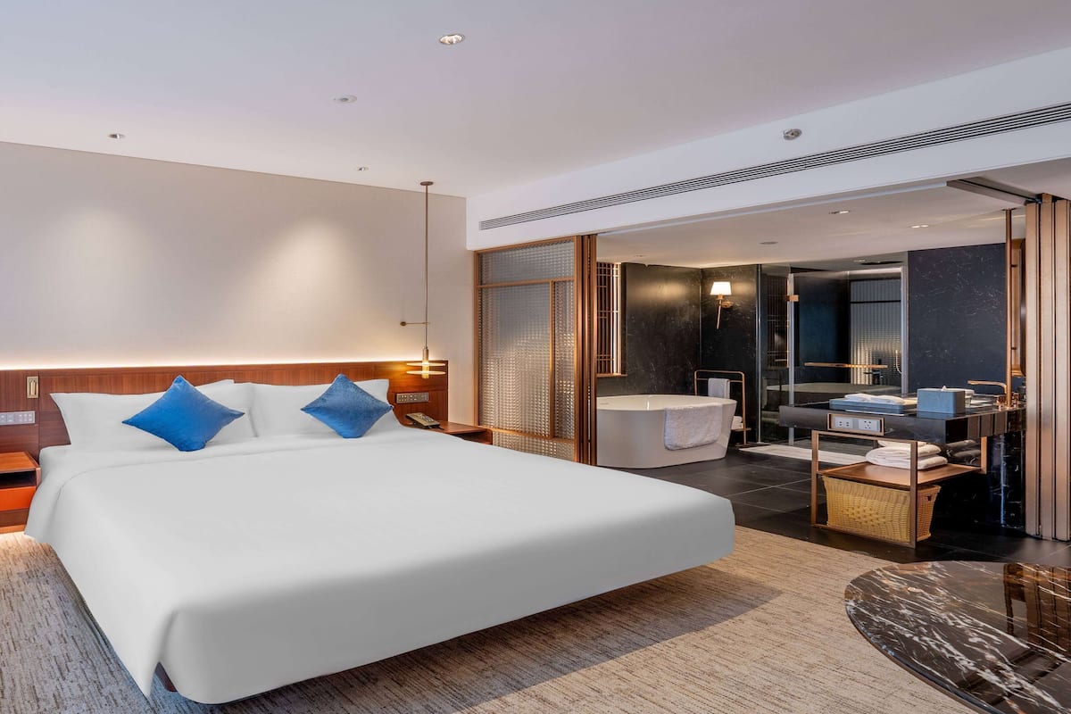 A modern hotel room with a large bed, a separate bathroom, and a small sitting area.