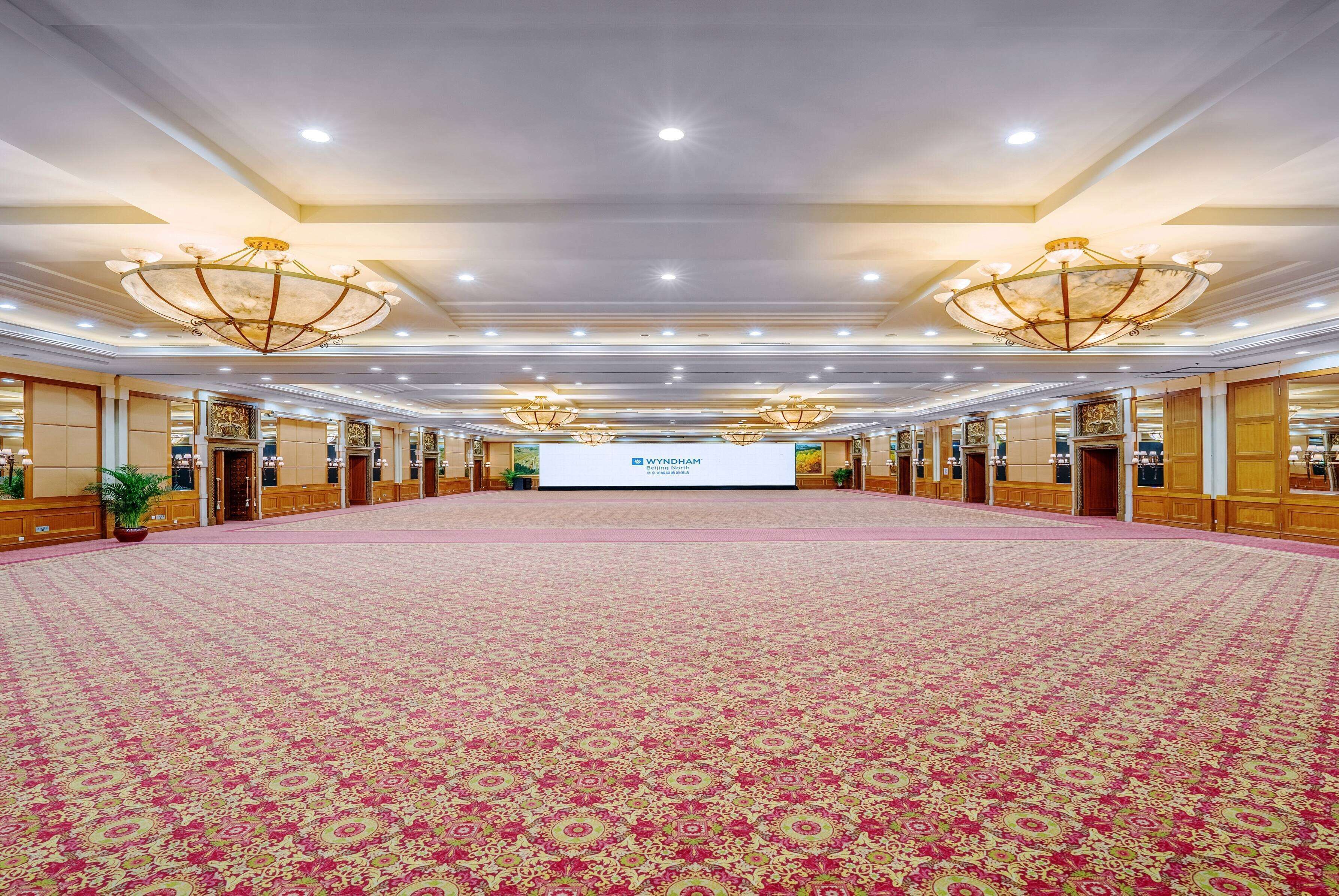 A large, well-lit conference room with a patterned carpet, chandeliers, and a podium at the front.