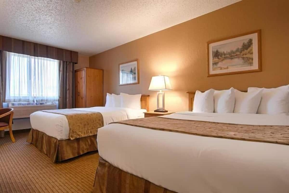A hotel room with two beds, a desk, a chair, a lamp, and a painting on the wall.