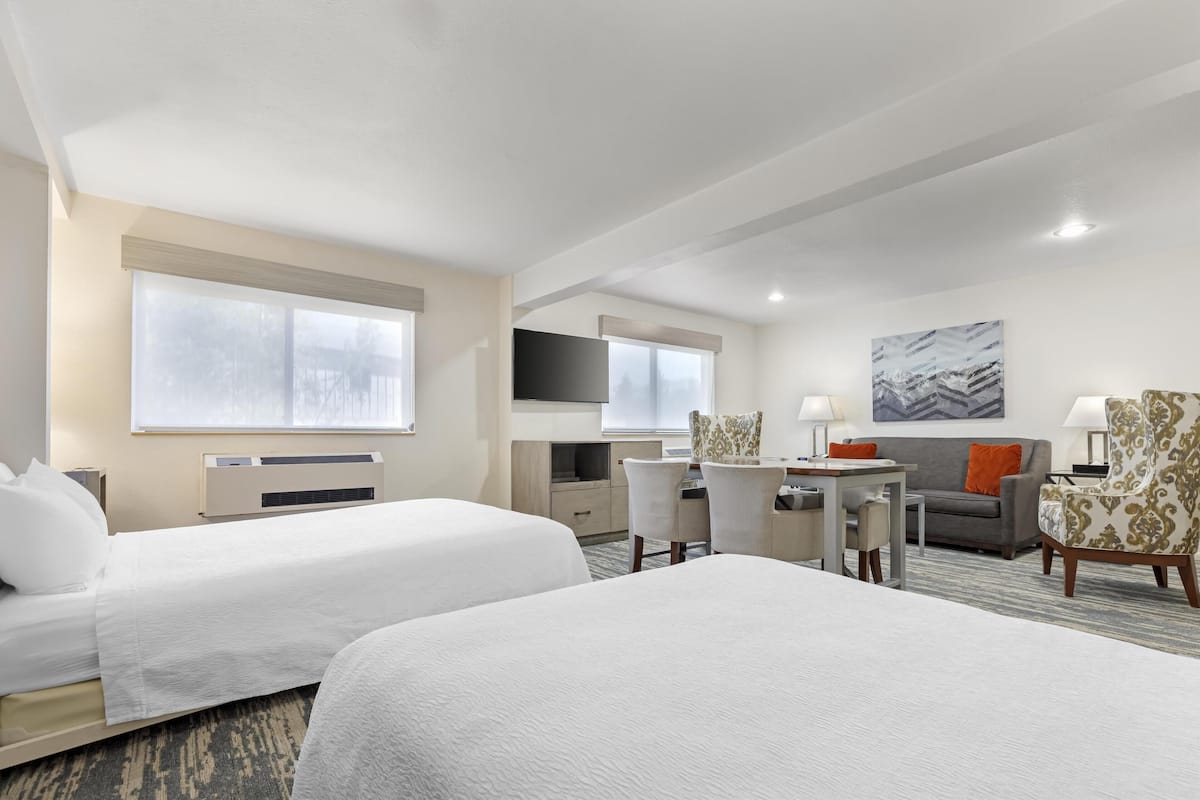 A hotel room with two beds, a desk, a sofa, and a TV.