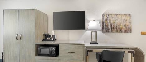 Une chambre d’hôtel comprenant un lit, un bureau avec une chaise, un téléviseur à écran plat, un four à micro-ondes, une lampe et un tableau au mur.