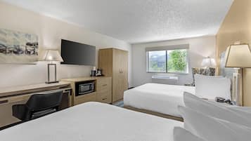 A hotel room with two beds, a desk with a television, a microwave, and a window with a view of greenery.