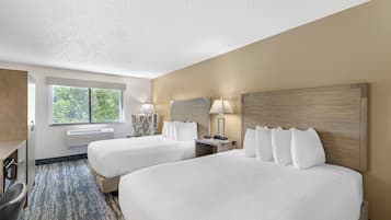 Une chambre d’hôtel avec deux lits, un bureau, une chaise, une fenêtre et un radiateur fixé au mur.