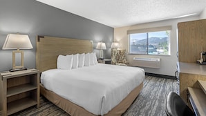 Habitación de hotel con una cama grande, dos mesitas de noche con lámparas, una silla, un escritorio y una ventana con vistas a las montañas.