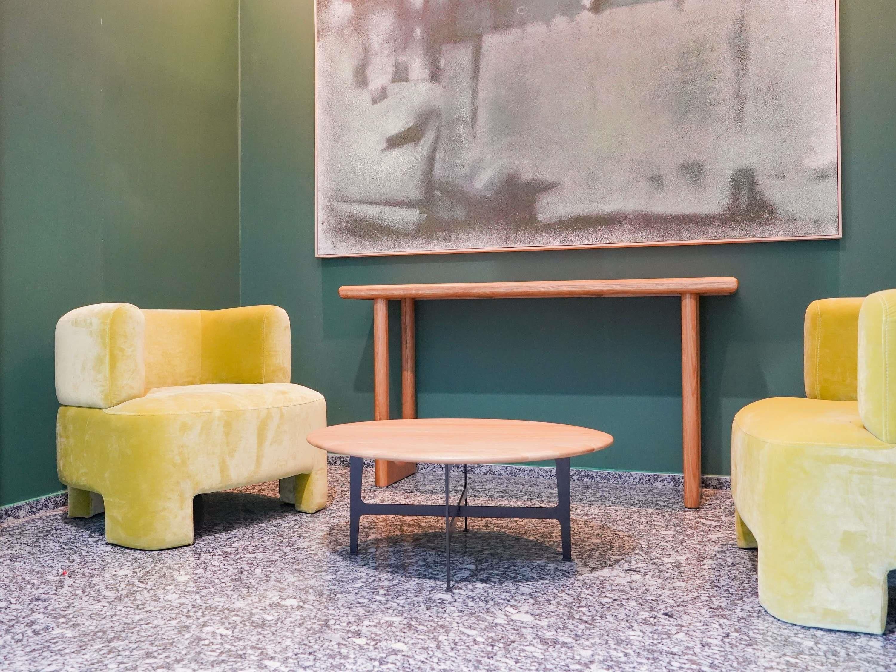 A room with a green wall, a painting, two yellow chairs, and a round table.