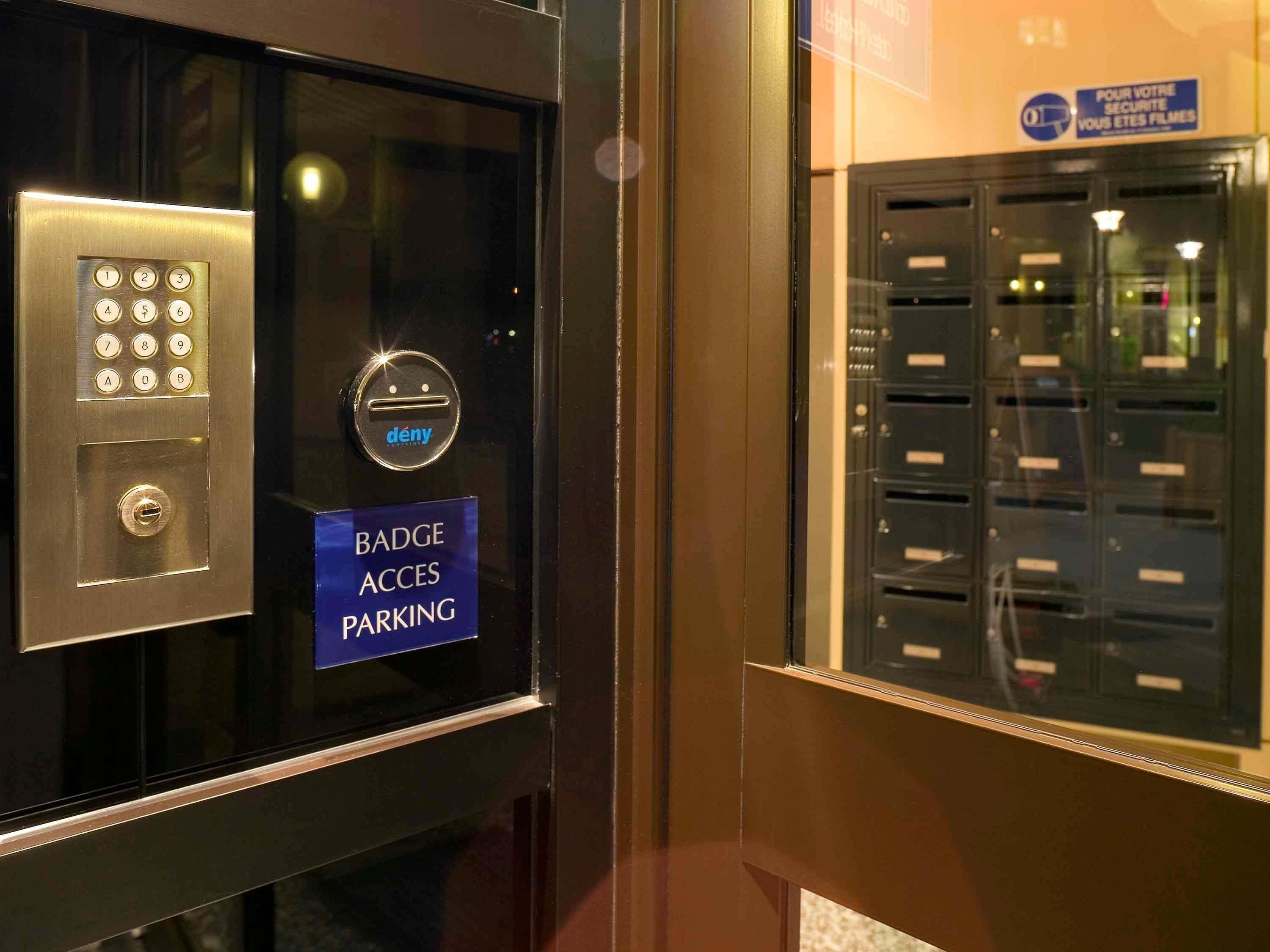 Un clavier de sécurité avec un panneau indiquant l’accès au parking par badge, un bouton « refuser » et une vue d’une fente à lettres sur laquelle est apposé un panneau.