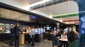 A modern bar area with a counter, seating, and a variety of bottles on shelves.