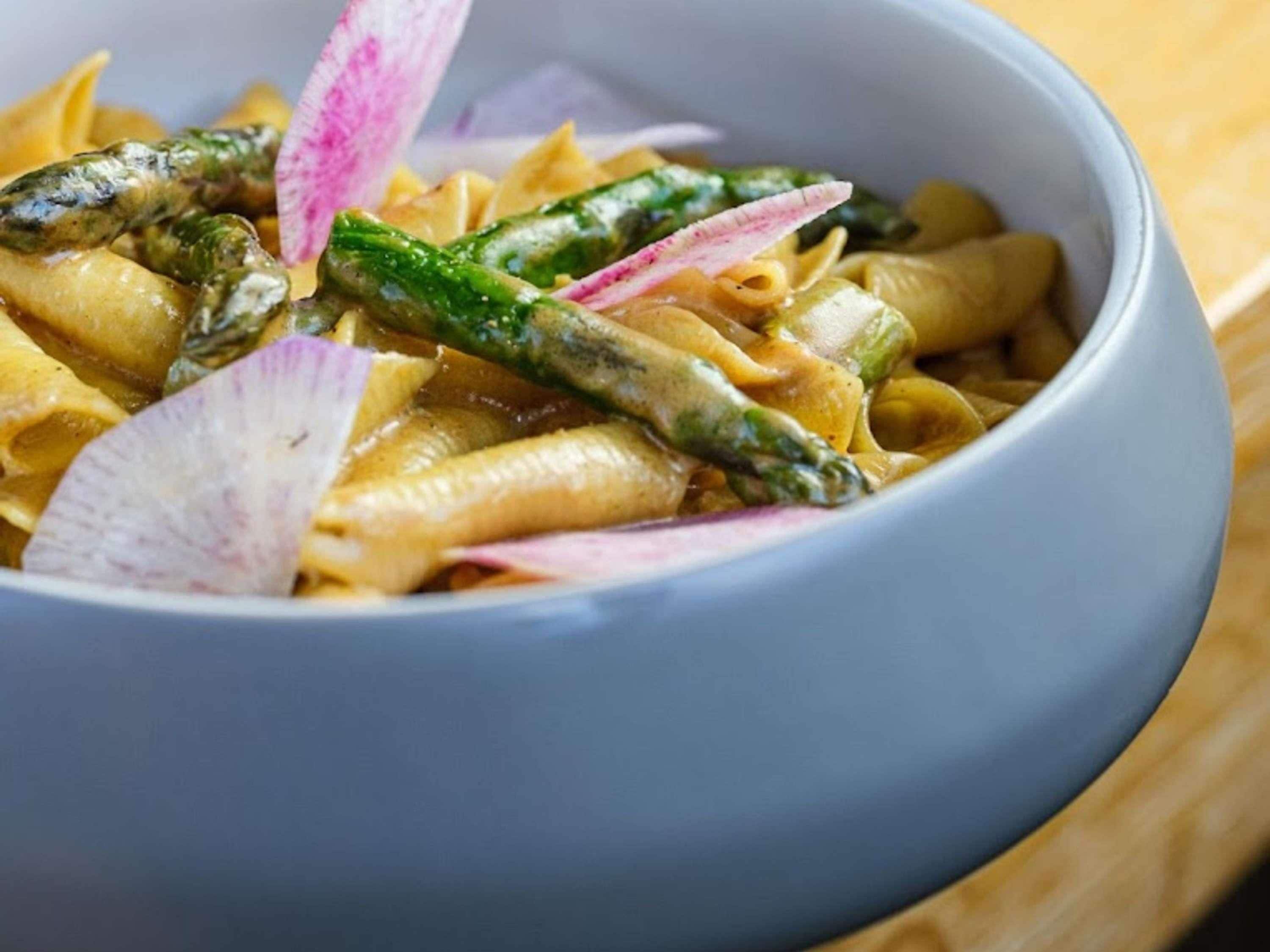 A bowl of pasta with asparagus and radish slices.