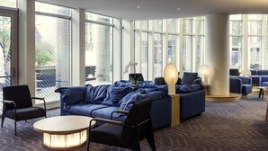 A modern lounge area with a blue sofa set, a round table, and a large window offering a view of the city.