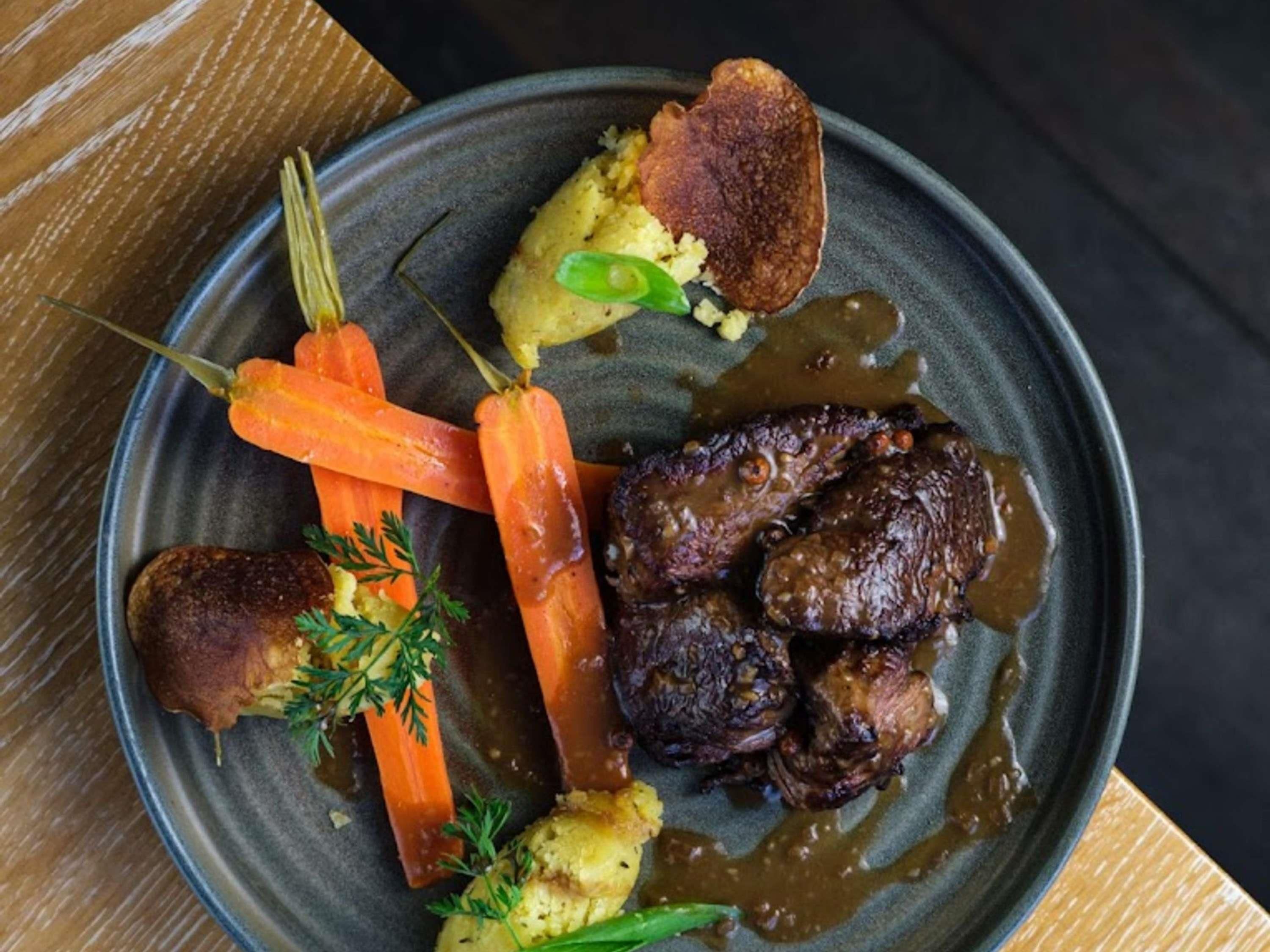 A plate of food with a piece of meat, carrots, and mashed potatoes.