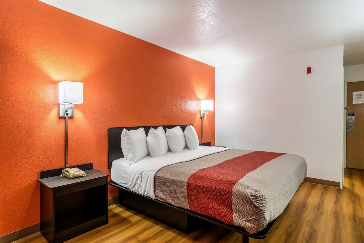 A hotel room with a bed, two bedside tables, a nightstand, and a red accent wall.