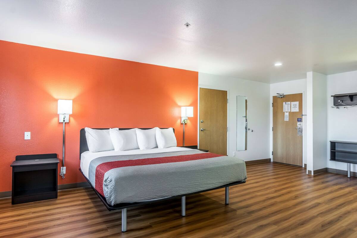 A hotel room with a bed, two bedside lamps, a wooden floor, a desk, and a door.