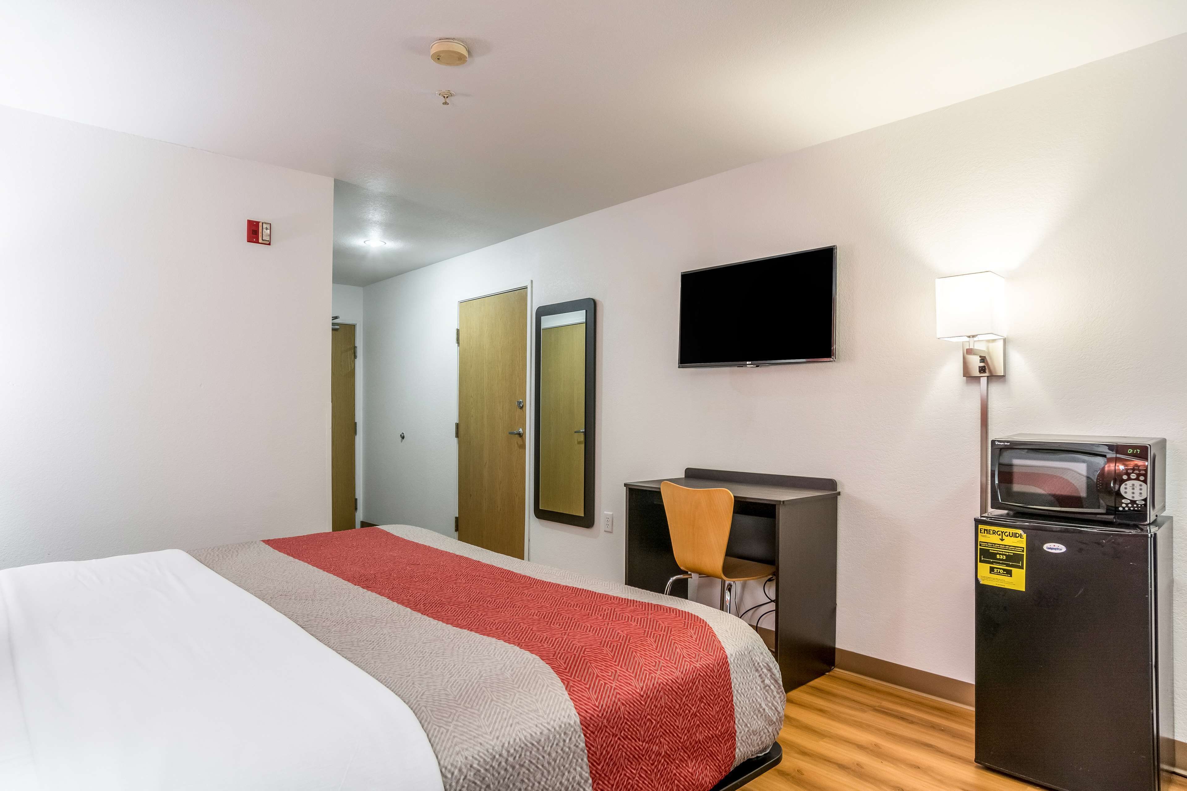 Una habitación de hotel con cama, escritorio, silla, televisor y refrigerador.