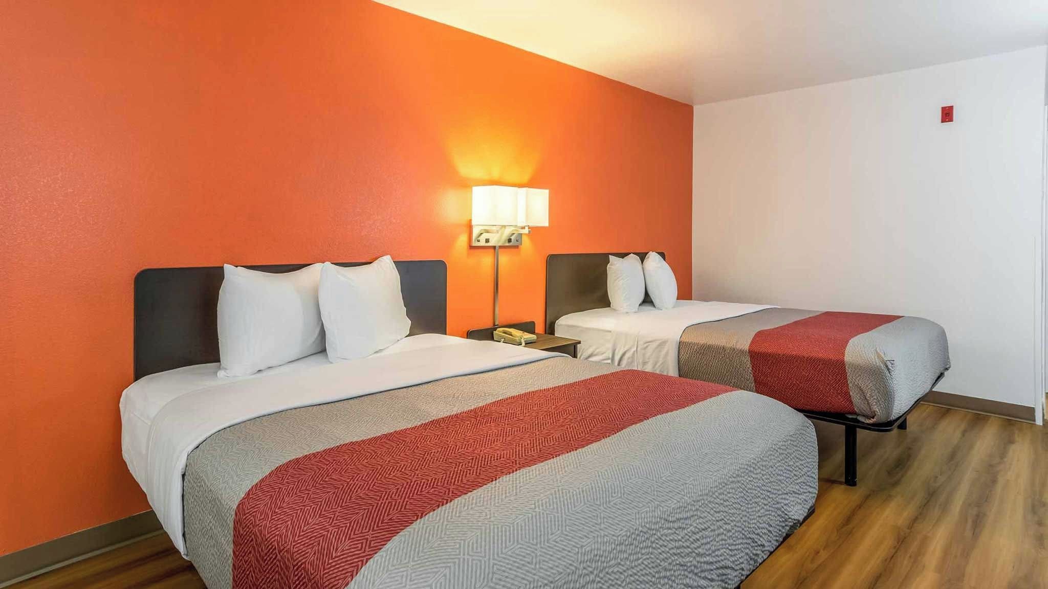 A hotel room with two beds, a nightstand, and a wall-mounted lamp.