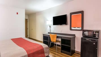Hotelkamer met een bed, bureau, stoel, televisie, magnetron en kleine koelkast.