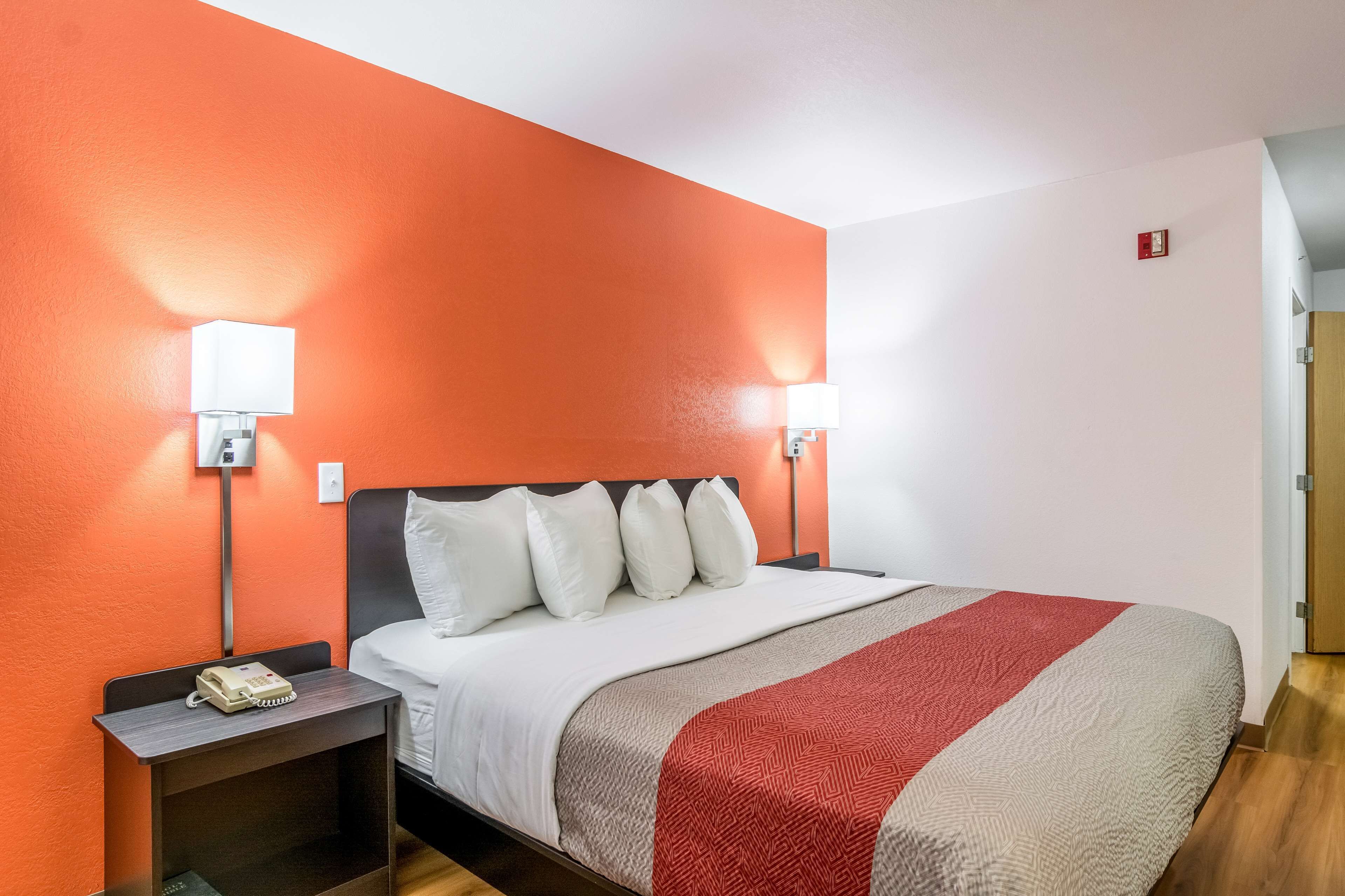 A hotel room with a large bed, two bedside tables, a telephone, and a red and white striped blanket.