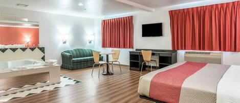 A hotel room with a bed, a sofa, a desk, a chair, a TV, and a bathtub.