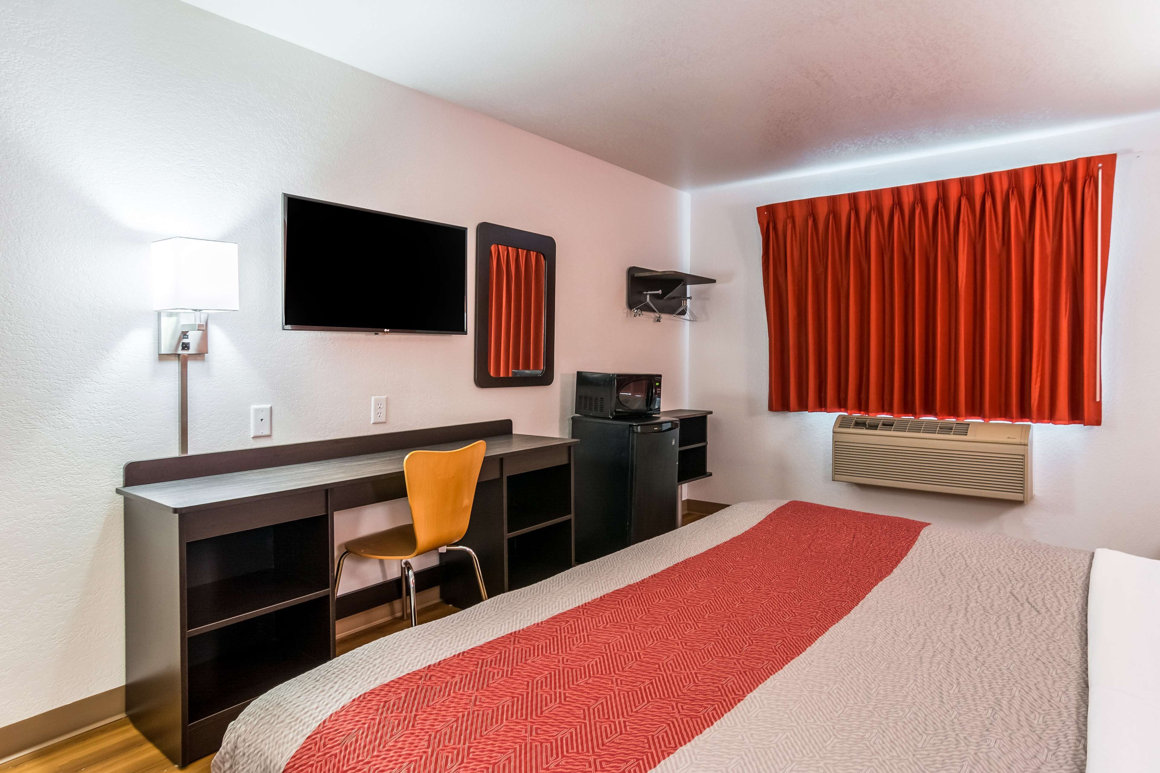 Habitación de hotel con cama, escritorio, silla, televisor y ventana con cortinas.