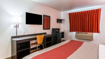 Habitación de hotel con cama, escritorio, silla, televisor y ventana con cortinas.