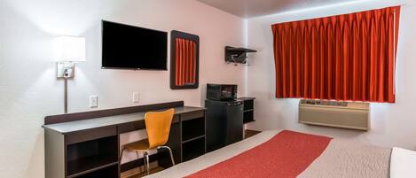 Habitación de hotel con cama, escritorio, silla, televisor y ventana con cortinas.