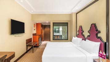 A hotel room with a large bed, a flat-screen TV mounted on the wall, a wooden bench, and a small table with bottles.