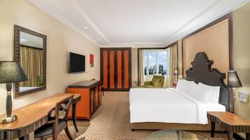 Habitación de hotel con cama, escritorio, silla, televisor y vista a la ciudad.