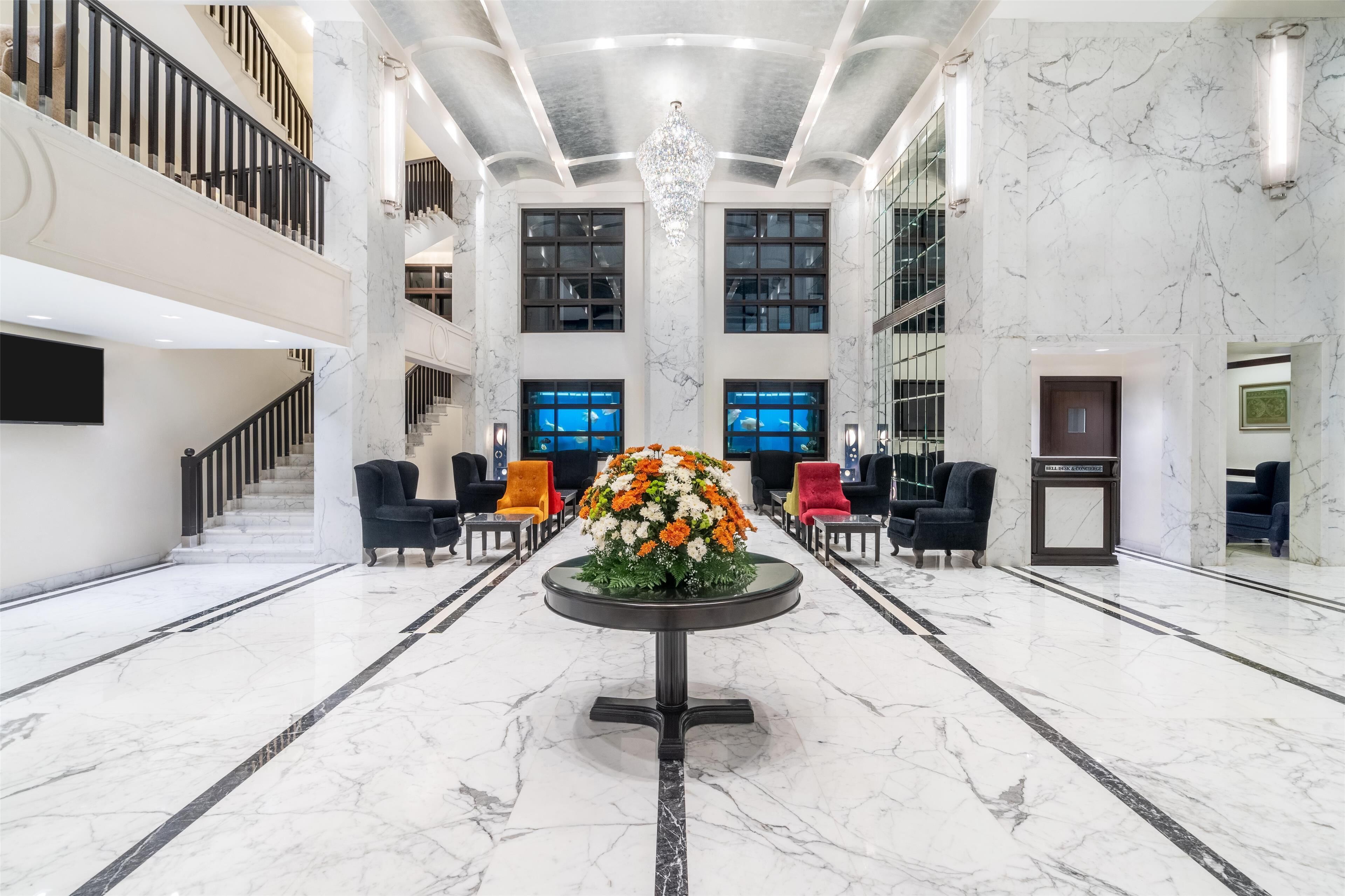 Un hall espacioso con suelos de mármol, un arreglo floral central, varias zonas de estar y una escalera que conduce a los pisos superiores.