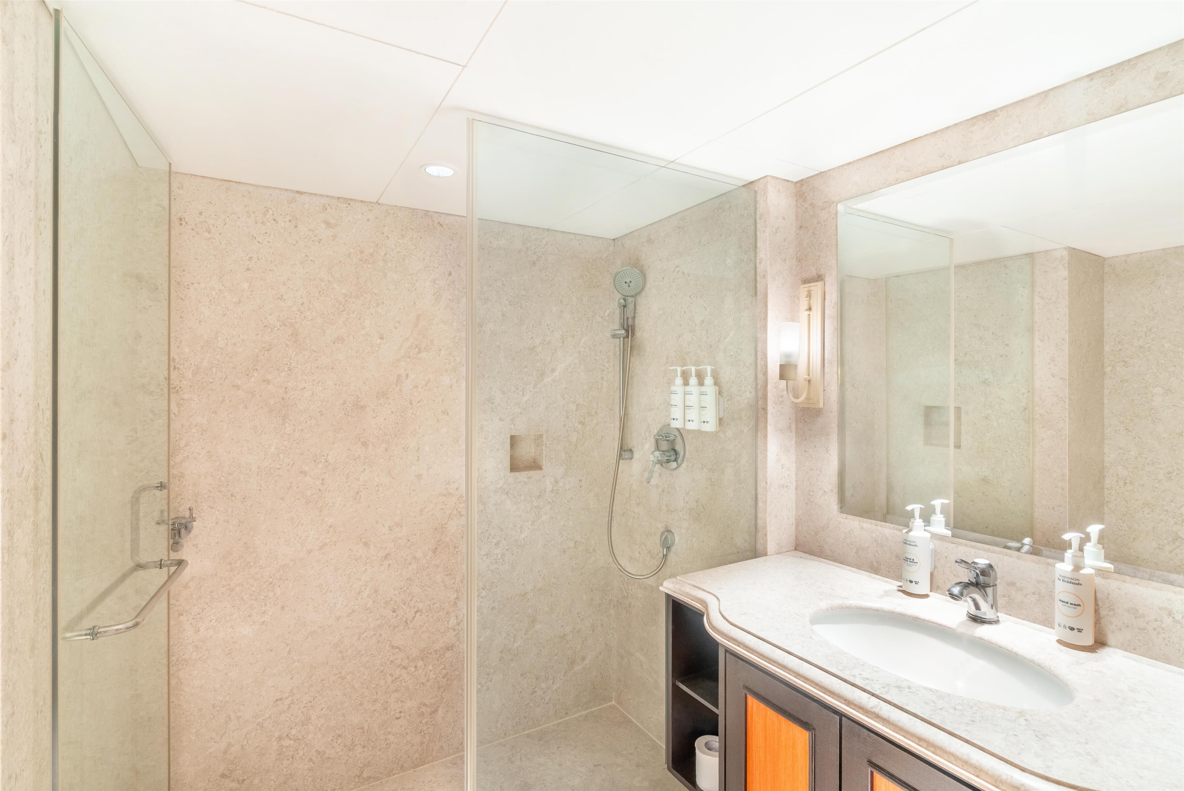 Un baño con cabina de ducha de vidrio, lavabo con espejo y artículos de aseo en la encimera.
