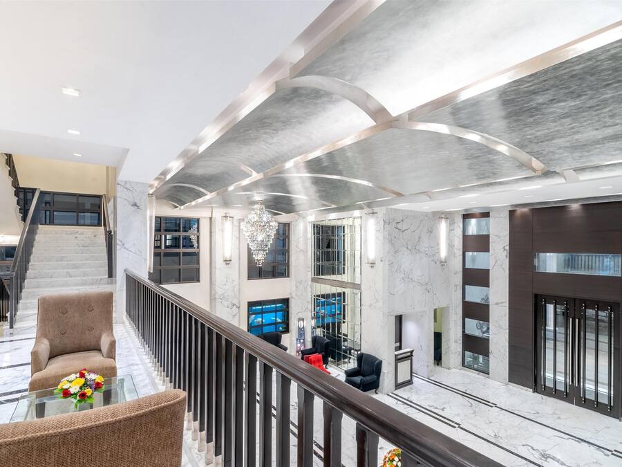 Un vestíbulo amplio con piso de mármol, una escalera y una zona de estar con una mesa de vidrio.