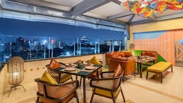 A rooftop dining area with a city view, furnished with leather chairs and tables, and a decorative hanging element.